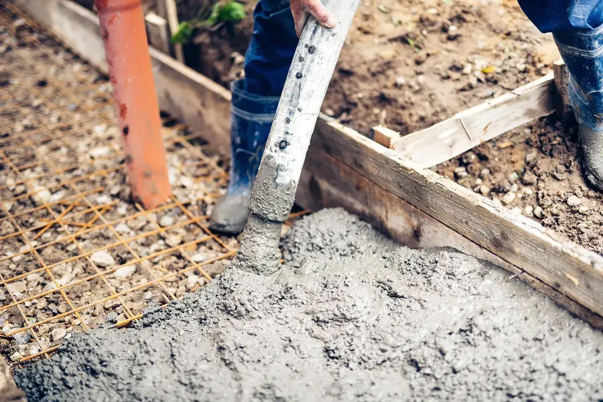 Arbeiter betonieren bei Regen eine Fundamentplatte. Beton fließt aus einem Schlauch auf eine Bewehrung.